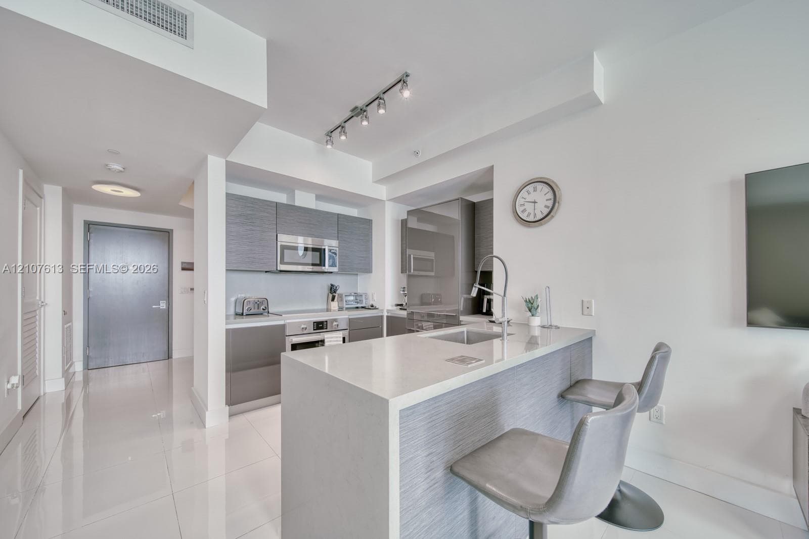 Kitchen featuring flat-panel grey cabinetry, quartz countertops, integrated stainless steel appliances, a breakfast bar with a high-arc faucet, and polished tile flooring