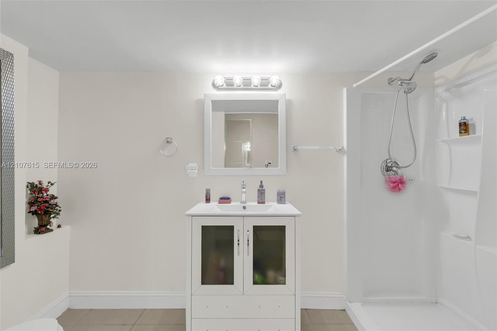 Bathroom featuring a white vanity with frosted glass cabinet doors, a rectangular undermount sink, a framed wall mirror, polished chrome hardware, and a walk-in shower enclosure