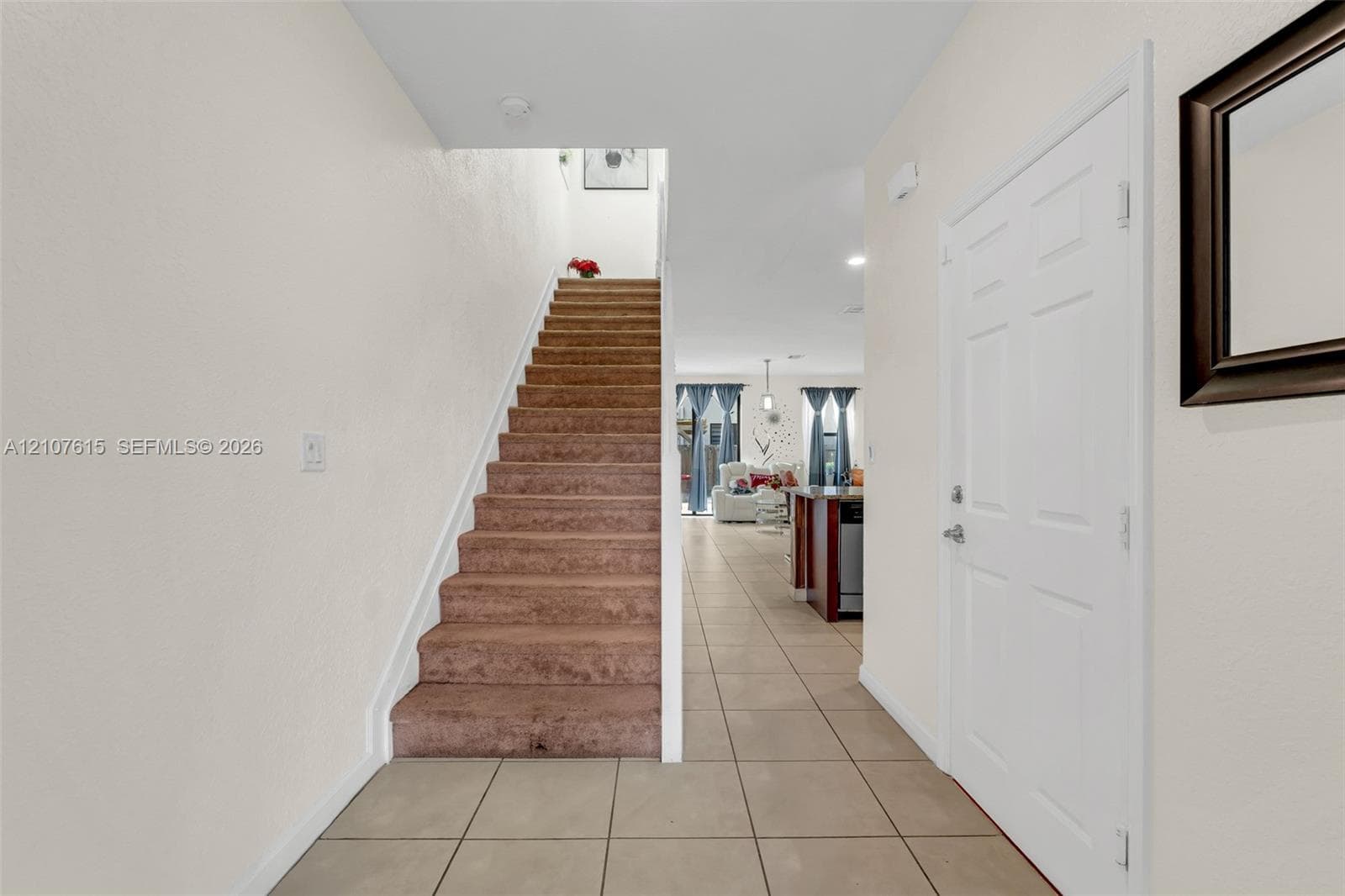 Entryway featuring large-format neutral floor tile, carpeted staircase with a crisp white handrail, and a six-panel entry door