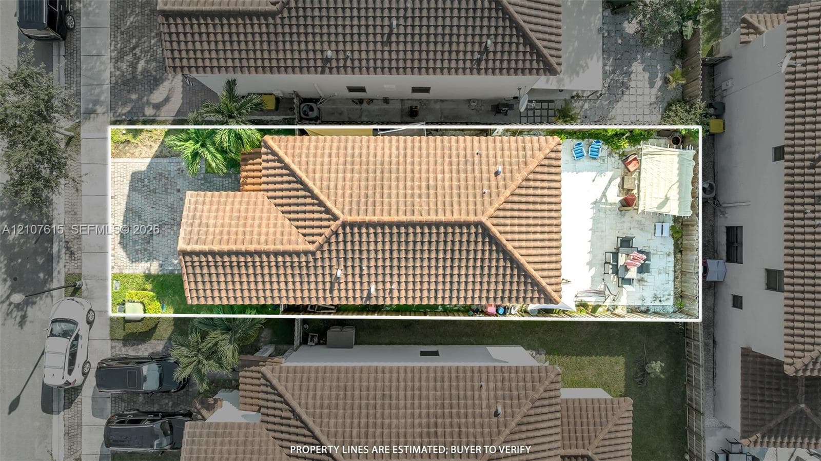 Aerial perspective featuring a tile roof, paved driveway, expansive concrete patio, and fenced perimeter