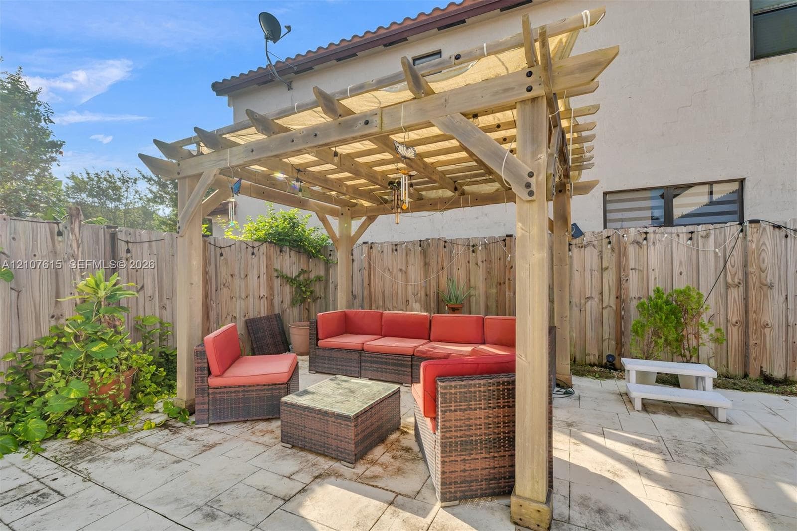 Rear patio featuring a wooden pergola with a fabric shade canopy and light-colored paver flooring, enclosed by a wood privacy fence