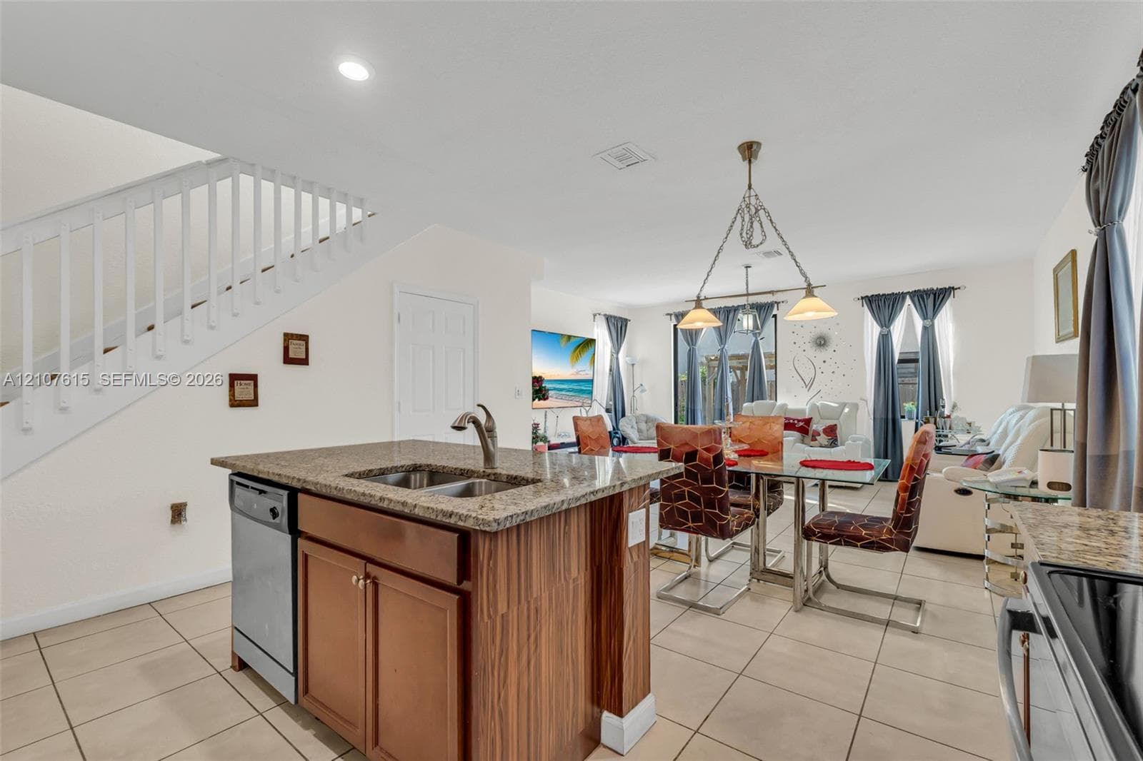 Kitchen island featuring a stone countertop, undermount double-basin sink, and wood-finish cabinetry, complemented by recessed lighting and tile flooring