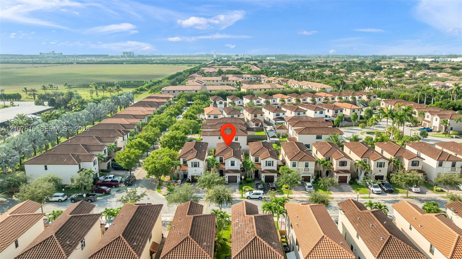 Aerial perspective of a multi-story residence featuring a terracotta-style tile roof and paved driveway, positioned within a suburban community with organized street layouts and green space