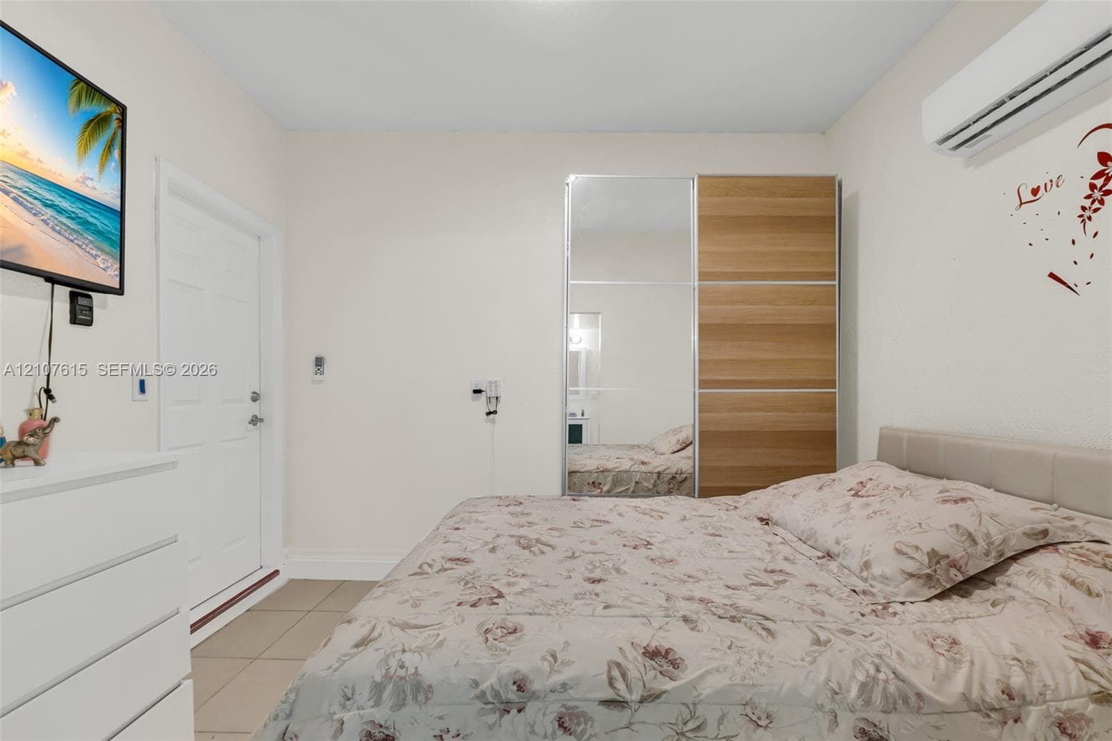 Wall-mounted ductless air conditioning unit, built-in floor-to-ceiling wardrobe with mirrored and wood-finish panels, and neutral tile flooring