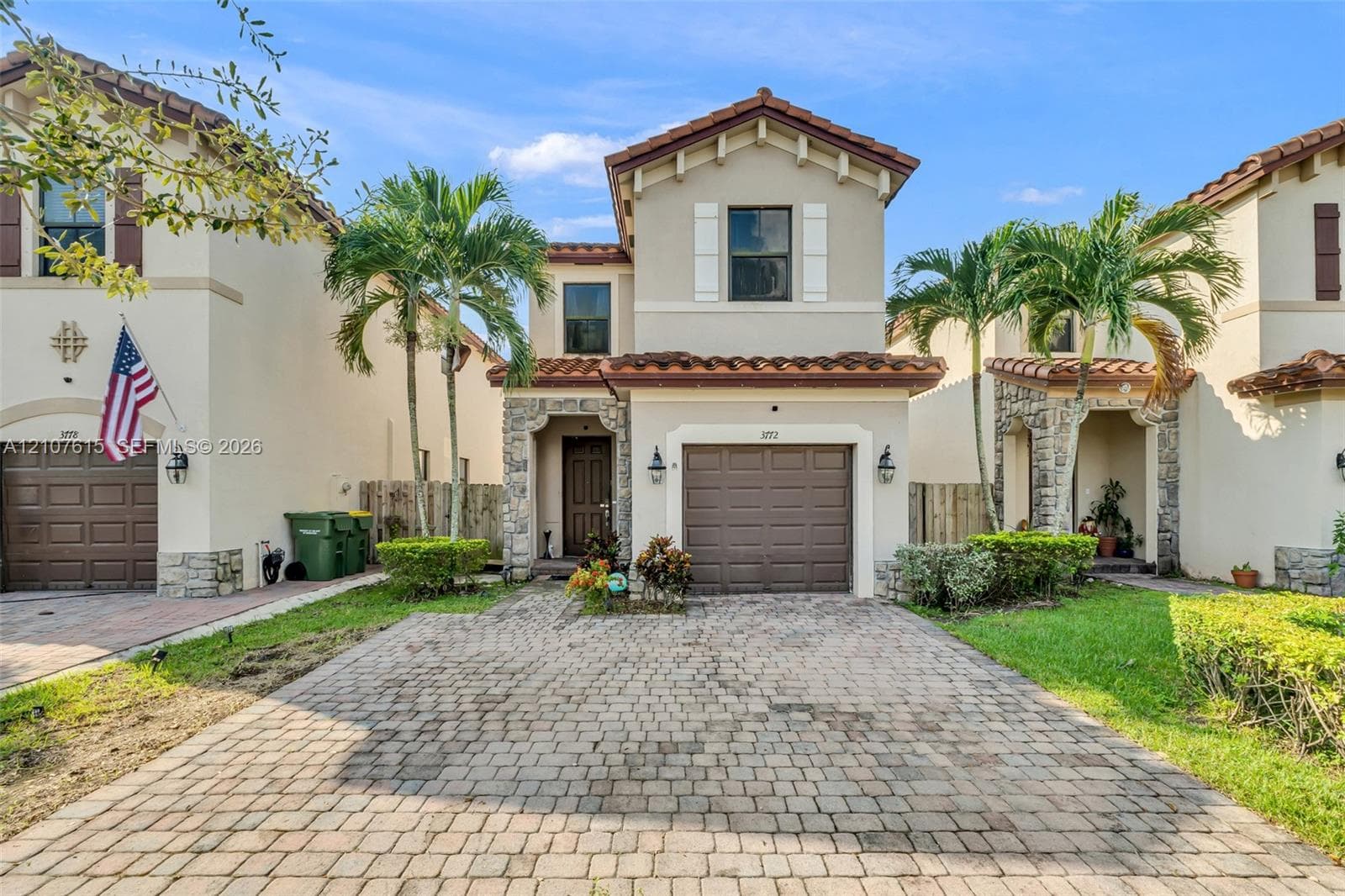 Two-story stucco exterior featuring stone veneer accents, a tiled roof, and a paved brick driveway