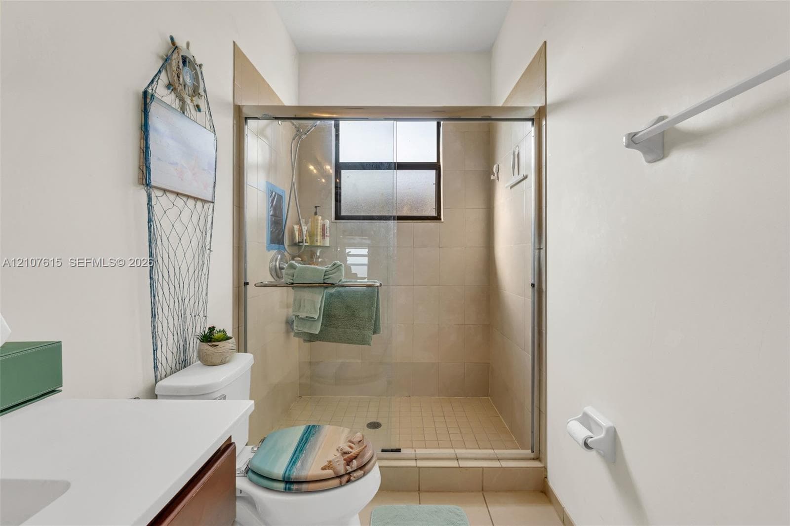 Walk-in shower with neutral tile surround, glass enclosure, handheld shower fixture, and tiled flooring