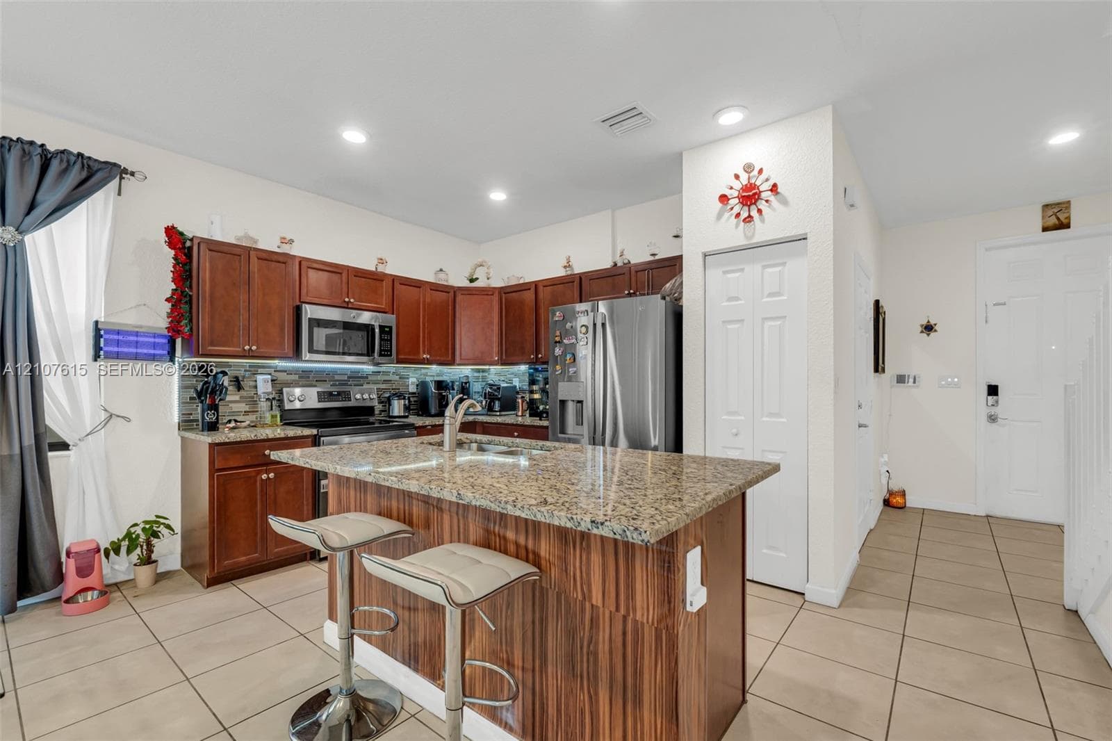 Kitchen featuring wood cabinetry, stone countertops, central island, stainless steel appliances, and tiled flooring