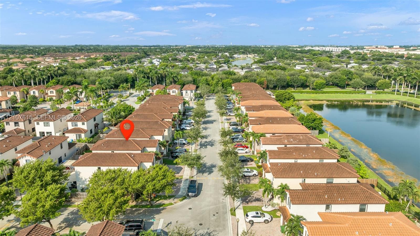 Aerial perspective of a multi-unit residential community featuring clay tile roof systems, stucco exteriors, and paved streets with mature landscaping
