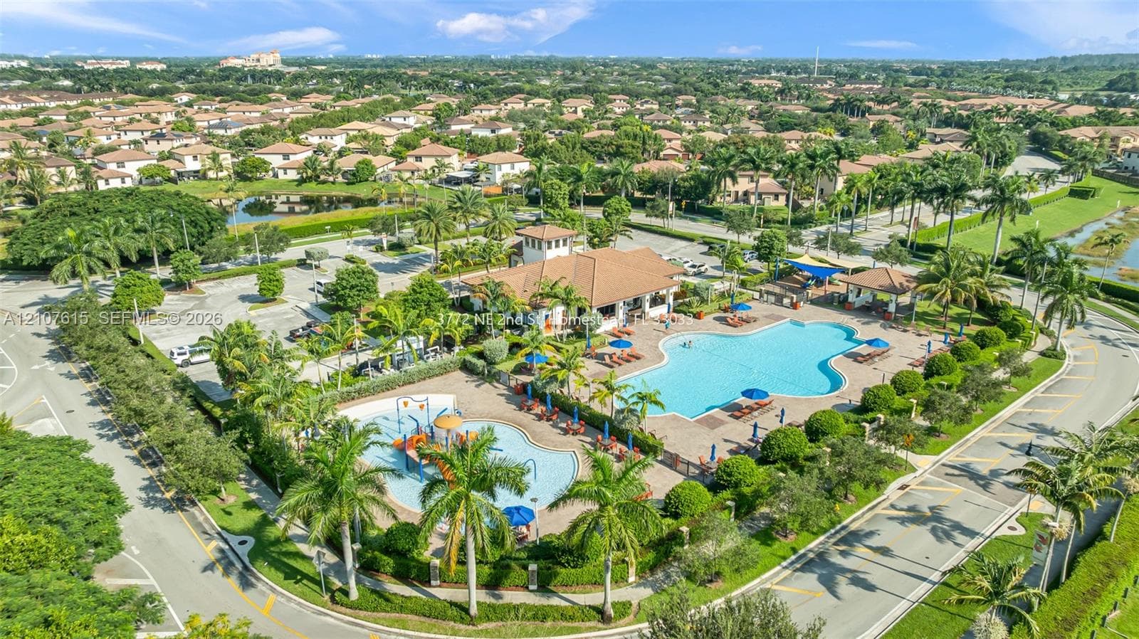 Community recreation area featuring a large swimming pool, shallow splash pool with water features, covered pavilion, and surrounding palm landscaping
