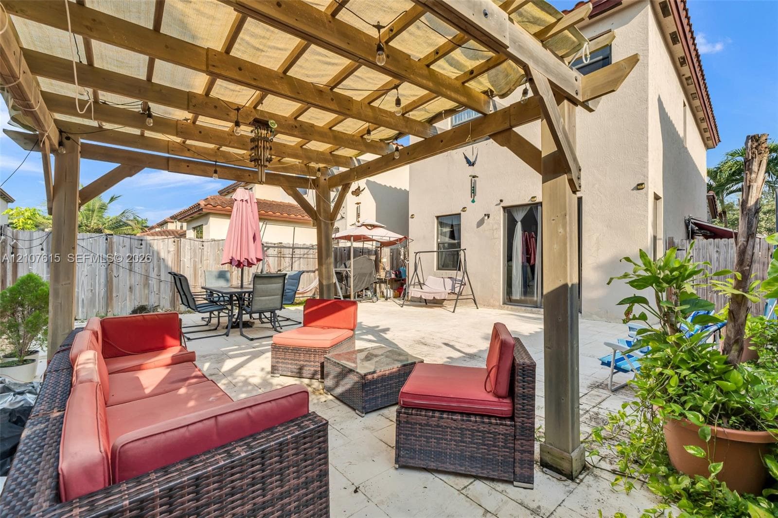 Backyard patio featuring a wood-beam pergola, light-toned stone paver flooring, and perimeter wood fencing