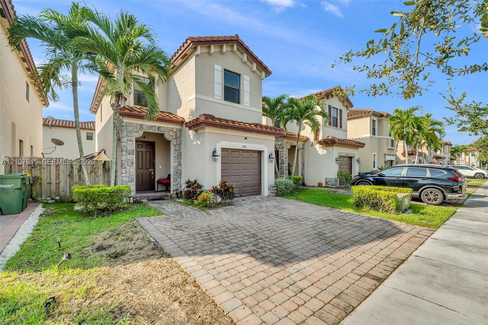 Two-story stucco exterior featuring a stone-clad entryway, decorative clay roof tiles, and a paved driveway