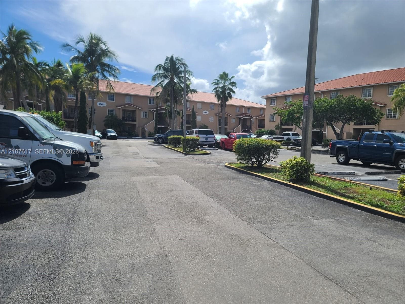 Multi-story stucco exterior featuring clay tile roofing, concrete paved parking areas, and established palm trees