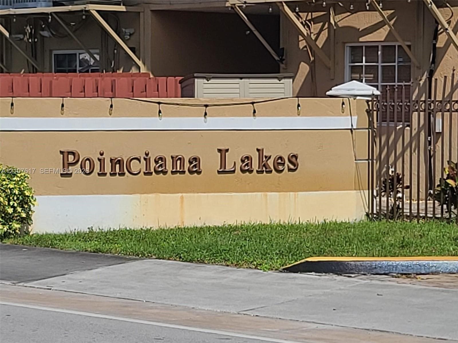 Stucco monument signage featuring dimensional lettering, landscaped greenery, and iron fencing