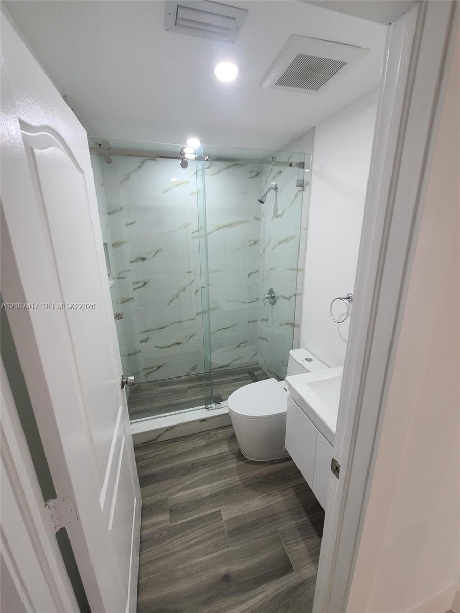 Walk-in shower with floor-to-ceiling stone-pattern tile, frameless glass sliding door, wood-finish flooring, and white floating vanity