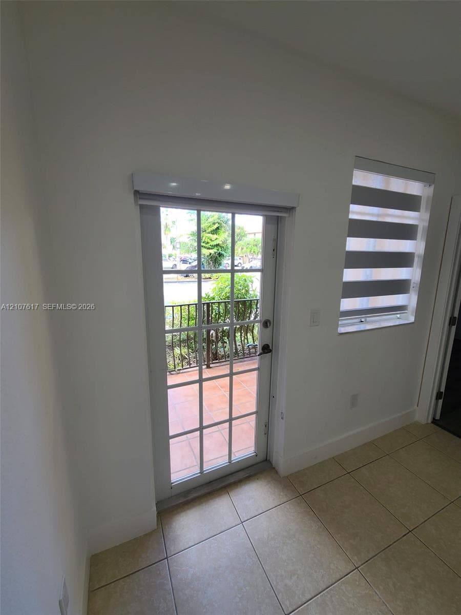 Full-light glass paneled door, tile flooring, and dual-layered roller window treatments