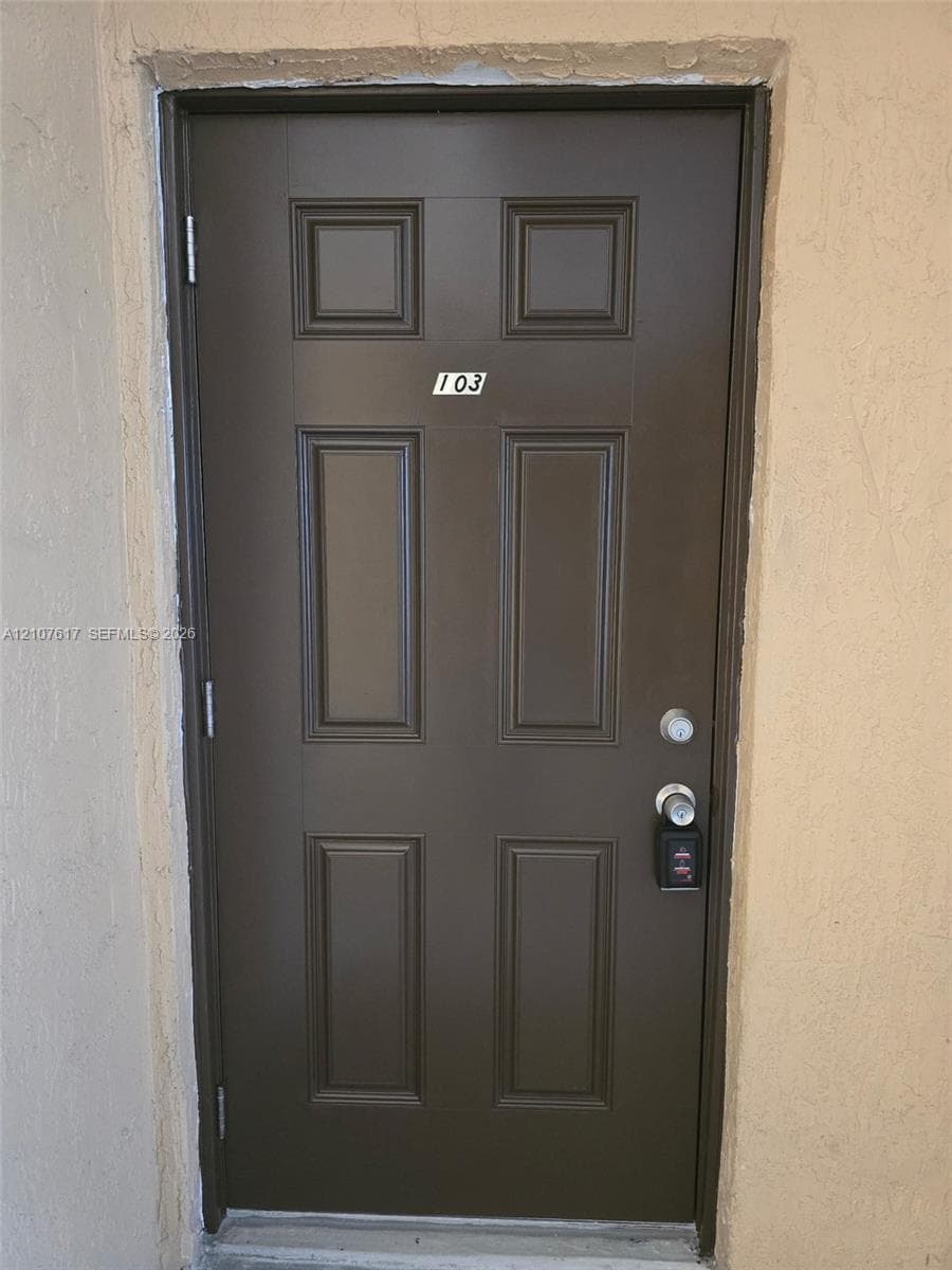 Six-panel brown entry door featuring a dual-lock system and textured wall surround