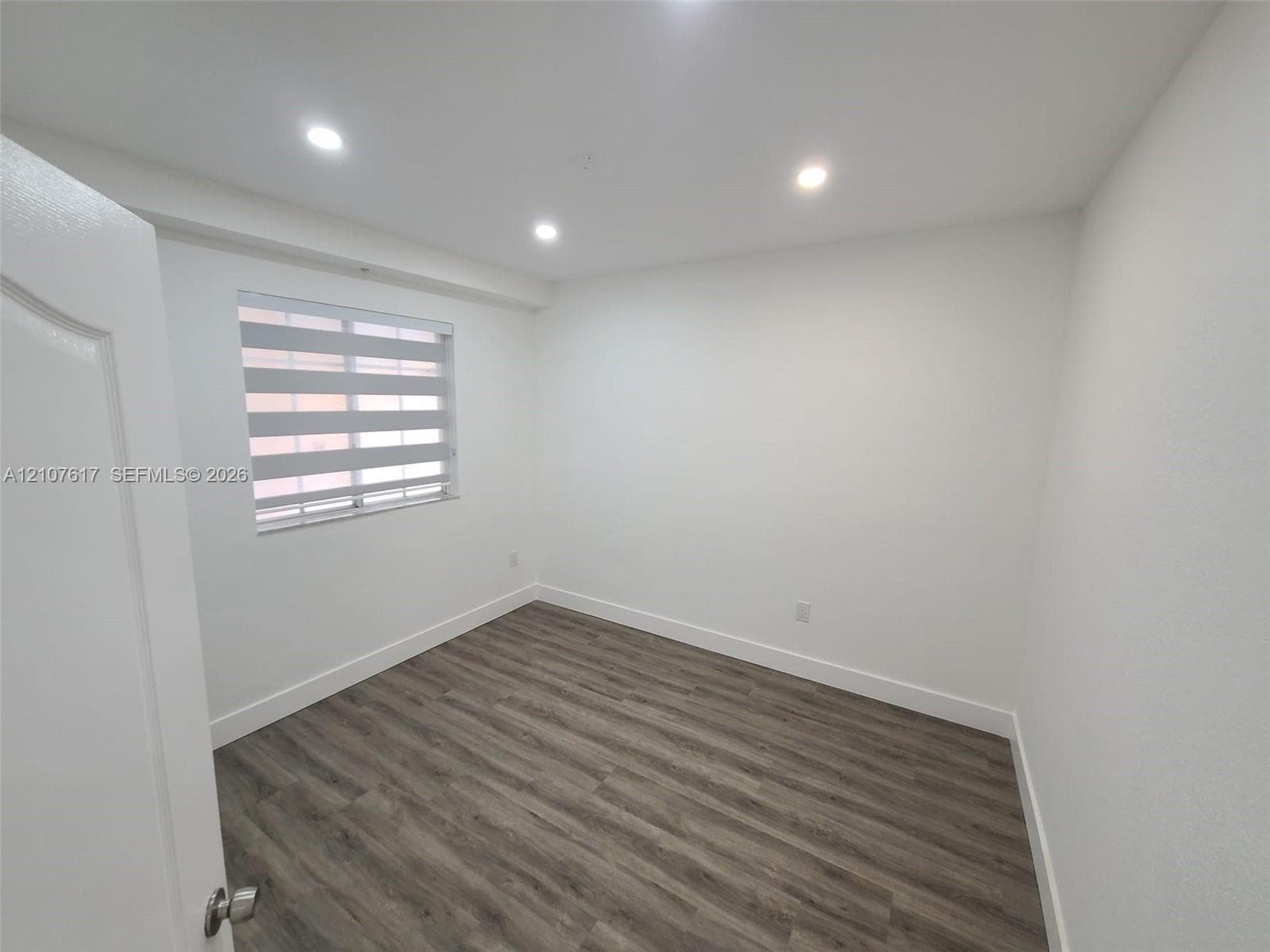 Interior room featuring wood-finish flooring, recessed lighting, and a window with horizontal shade blinds