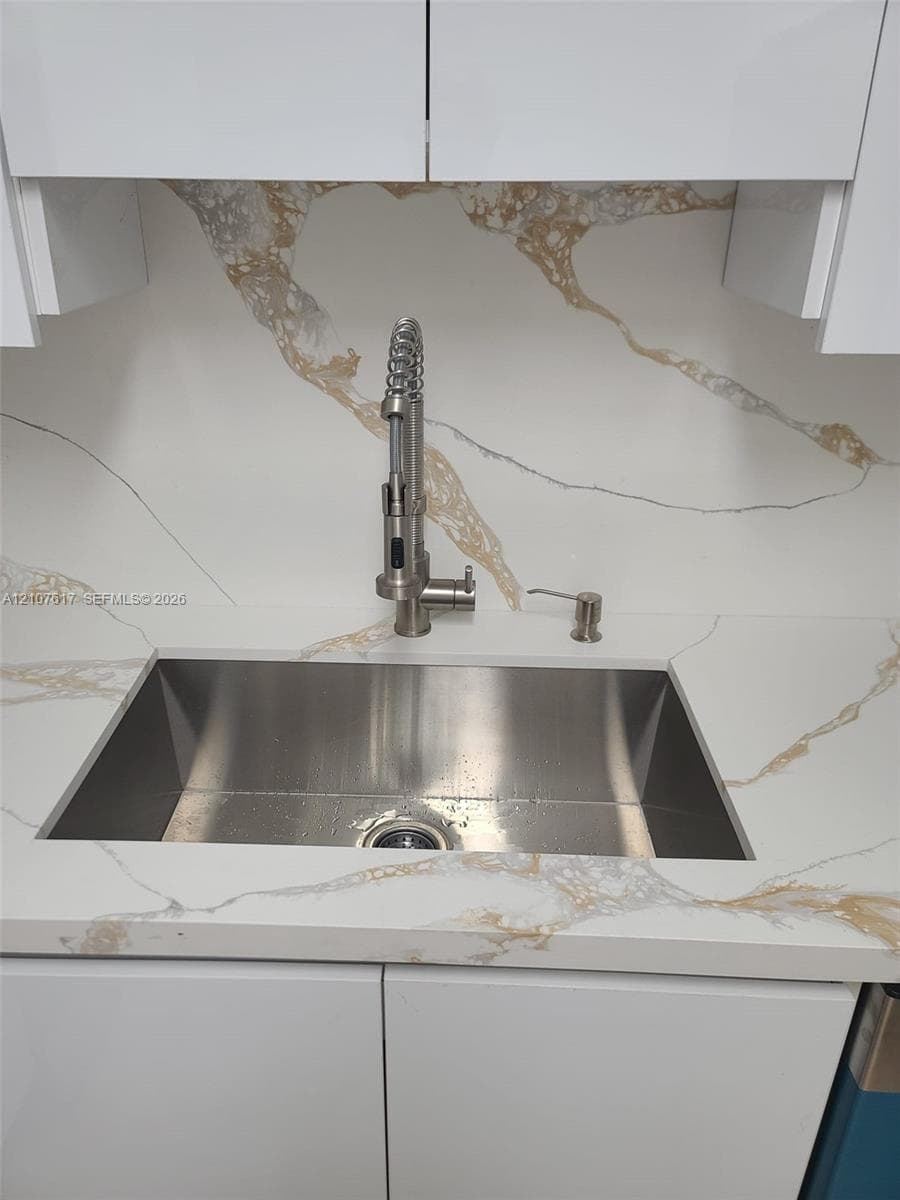 Undermount stainless steel sink featuring a high-arc pull-down sprayer faucet, integrated soap dispenser, and patterned stone-finish countertop and backsplash with white high-gloss cabinetry
