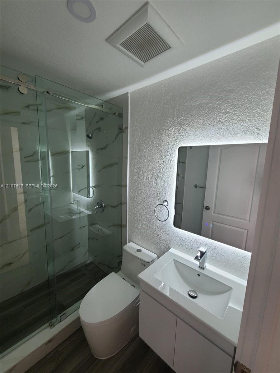 Glass-enclosed shower with tiled walls, modern vanity with rectangular basin, back-lit mirror, and wood-finish flooring