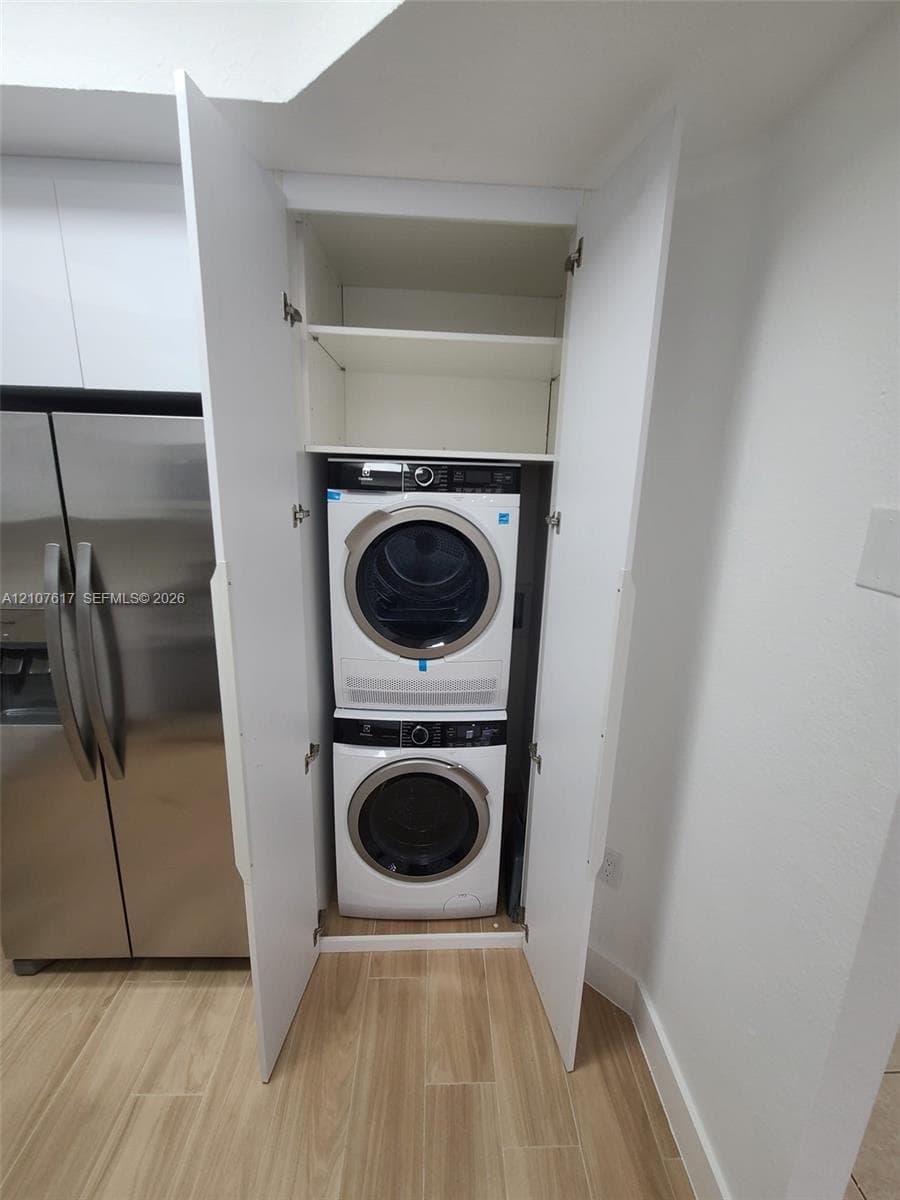 Built-in laundry closet with stacked washer and dryer, integrated shelving, and wood-finish flooring