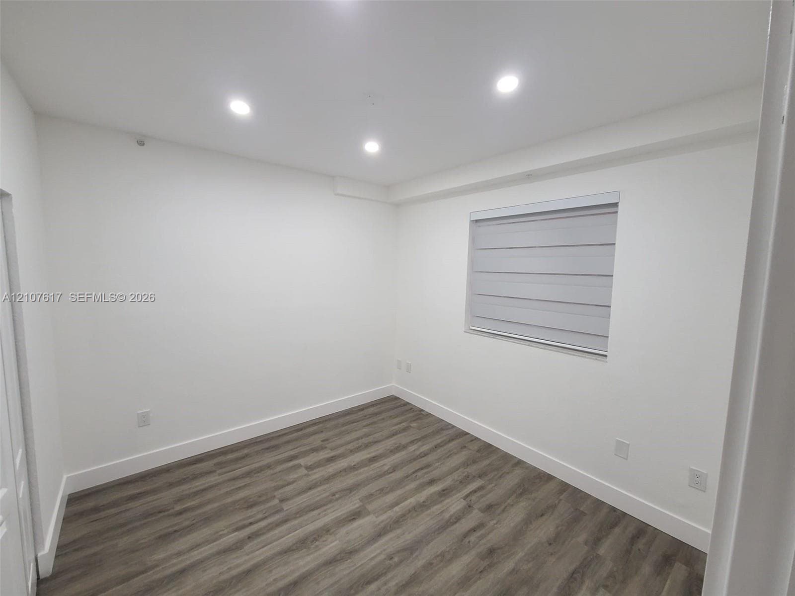 Interior room featuring wood-finish flooring, recessed lighting, and a window with a fitted roller shade