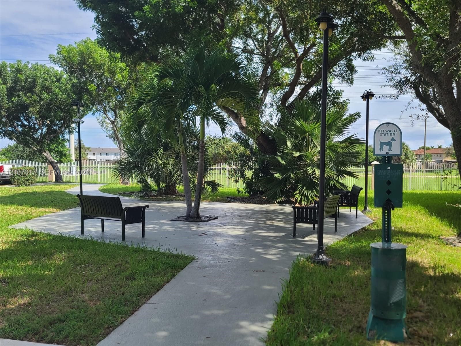 Landscaped common area featuring paved pathways, metal benches, mature palm trees, and integrated lighting fixtures