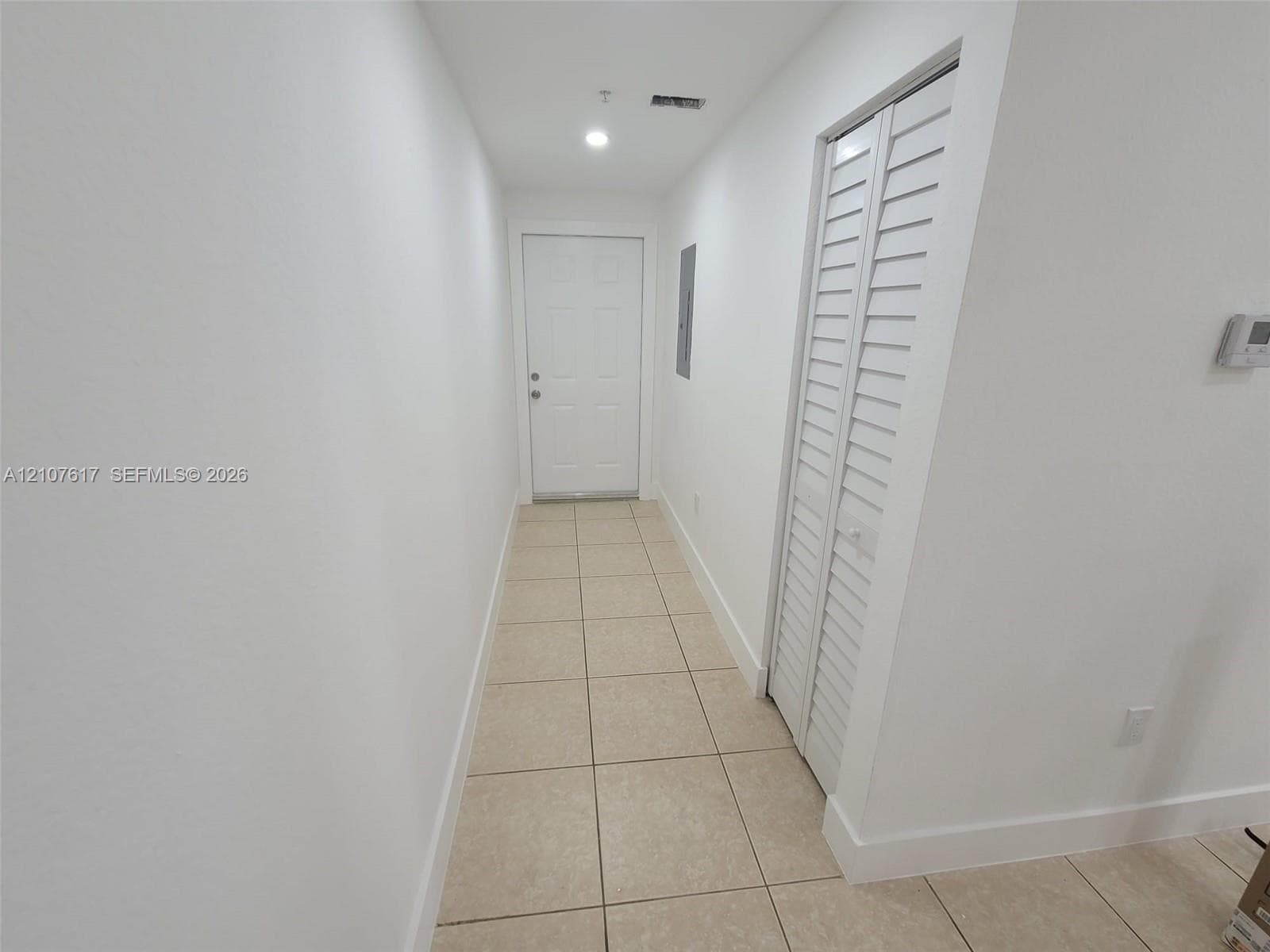 Interior hallway featuring neutral ceramic tile flooring, a six-panel door, and closet doors with louvered panels