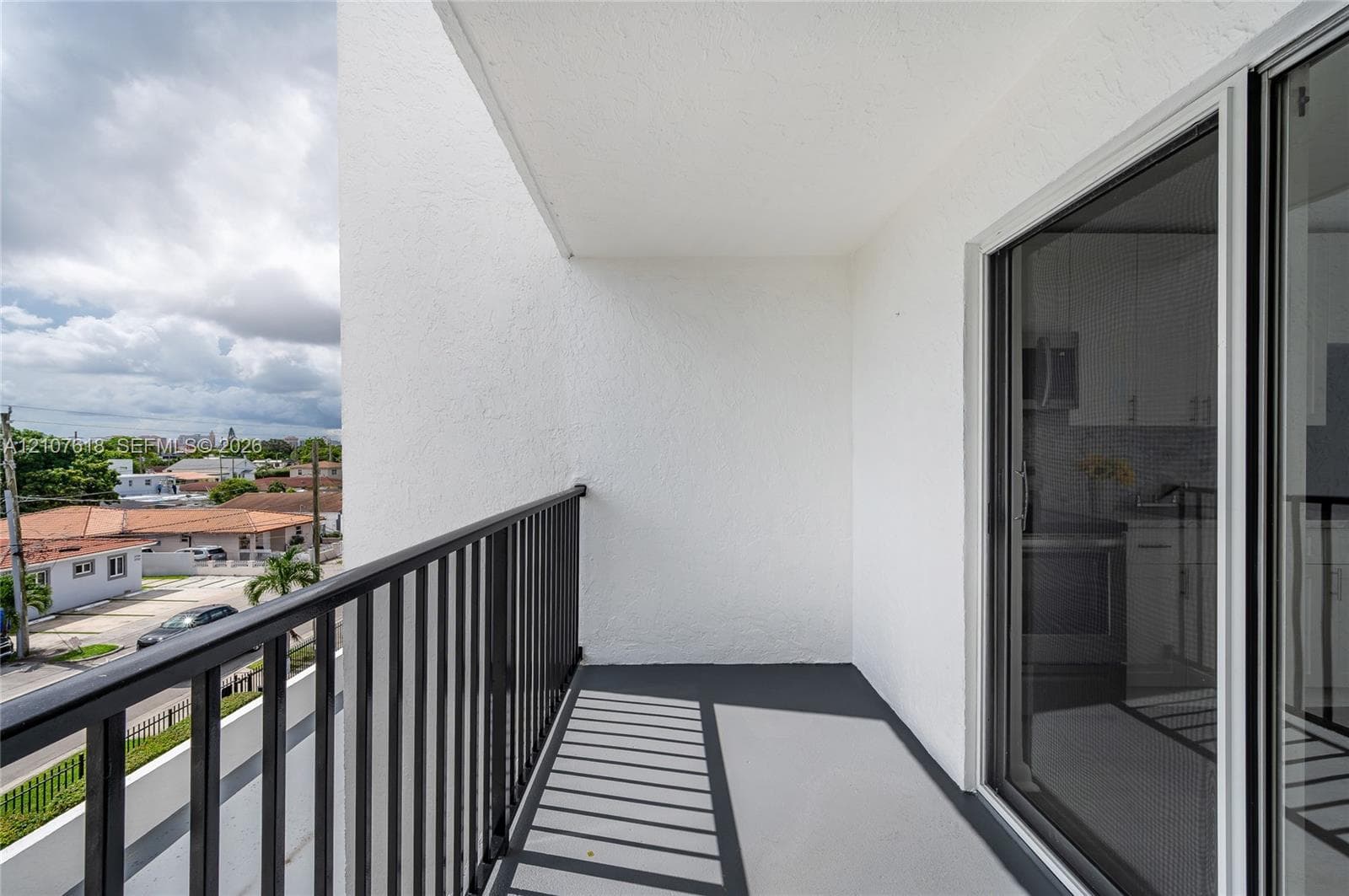 Private balcony featuring smooth stucco walls, concrete flooring, and black metal railings
