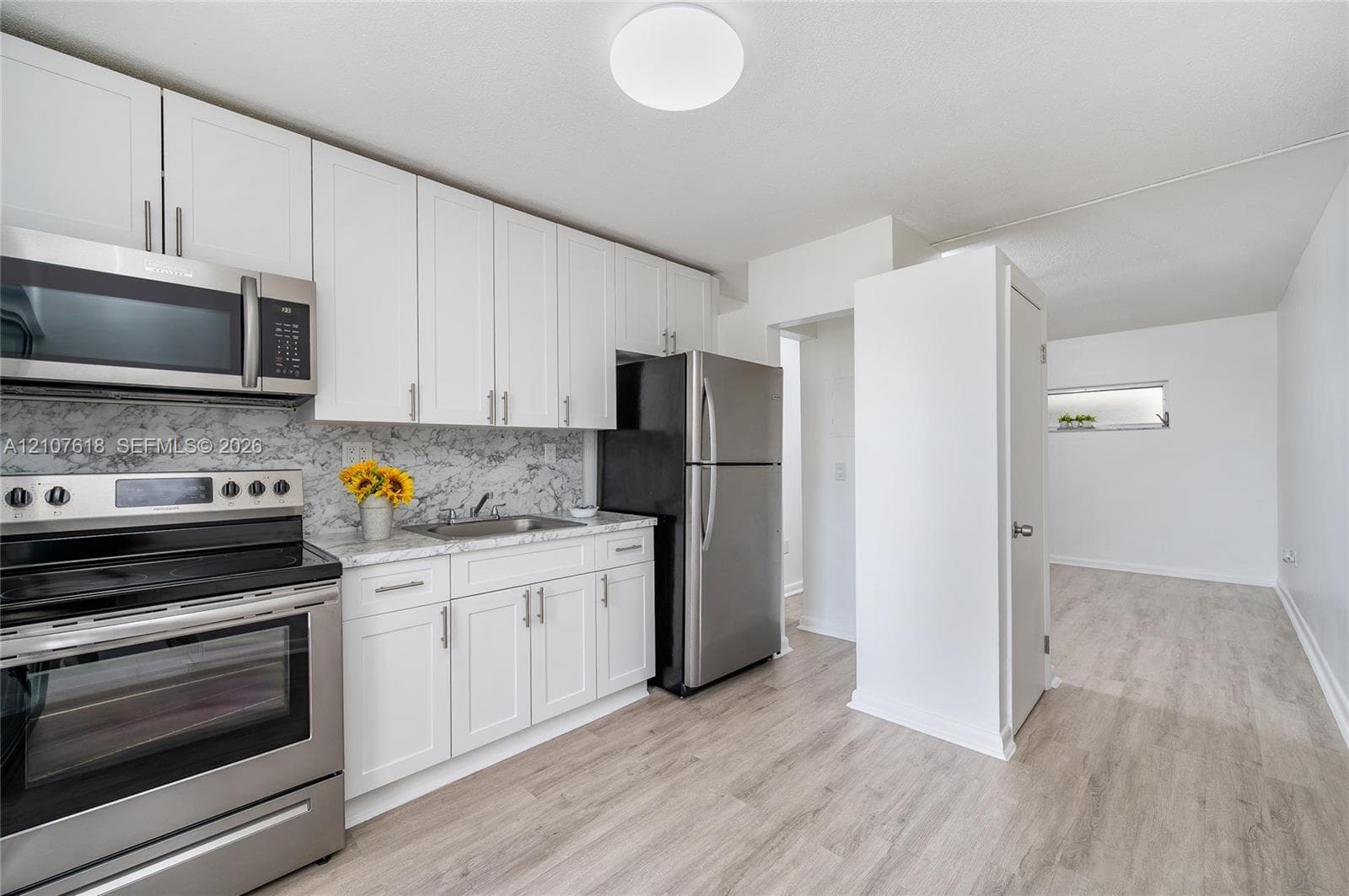 Kitchen featuring white shaker-style cabinetry, stone-finish countertops, full-height decorative backsplash, stainless steel appliances, and wood-finish flooring