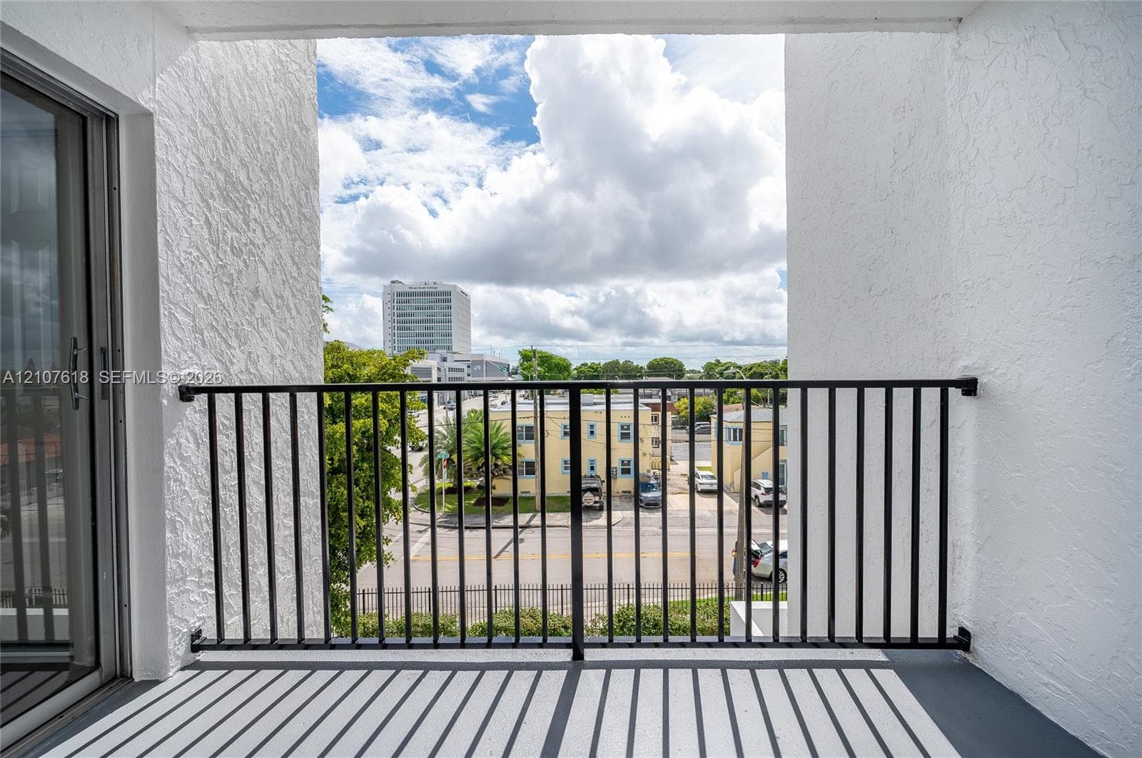 Covered balcony with textured stucco walls, black metal railing, and sliding glass entry door