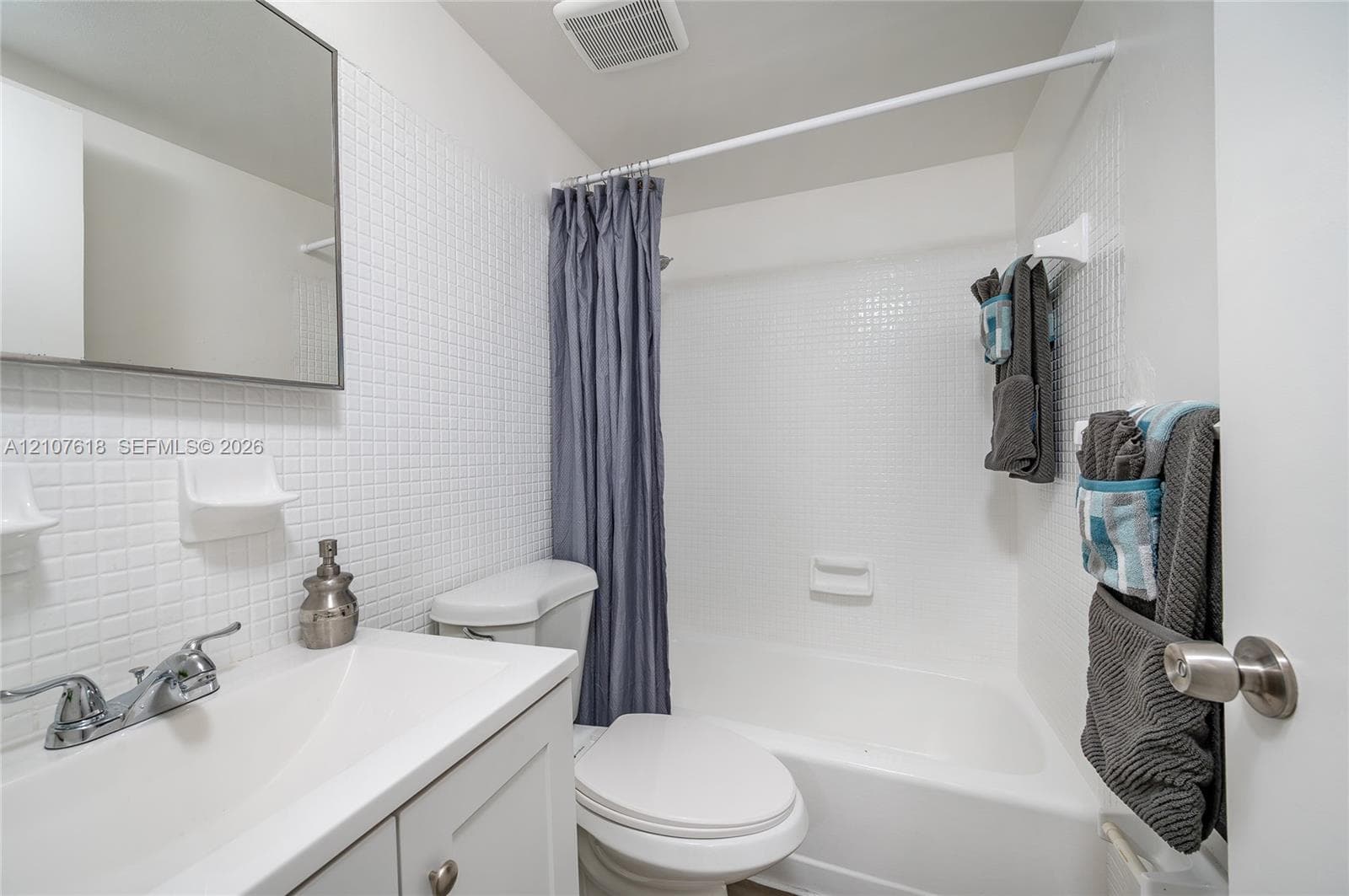 Bathroom featuring a white vanity cabinet, rectangular undermount sink, chrome faucet, tiled wall surfacing, and a built-in shower and tub combination
