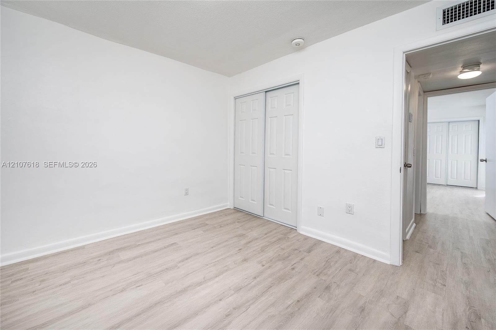 Room featuring wood-finish flooring, white walls, and a closet with dual-panel sliding doors