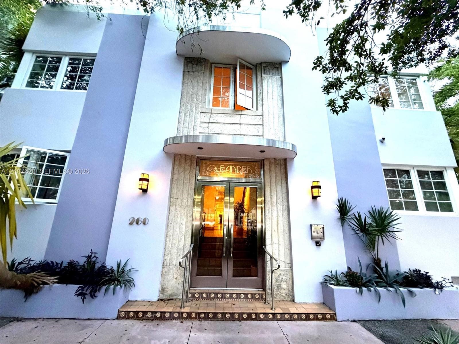 Art Deco facade featuring geometric stonework, a stepped entrance with decorative tile detailing, double-glass entry doors, integrated wall-mounted lighting, and metal awnings