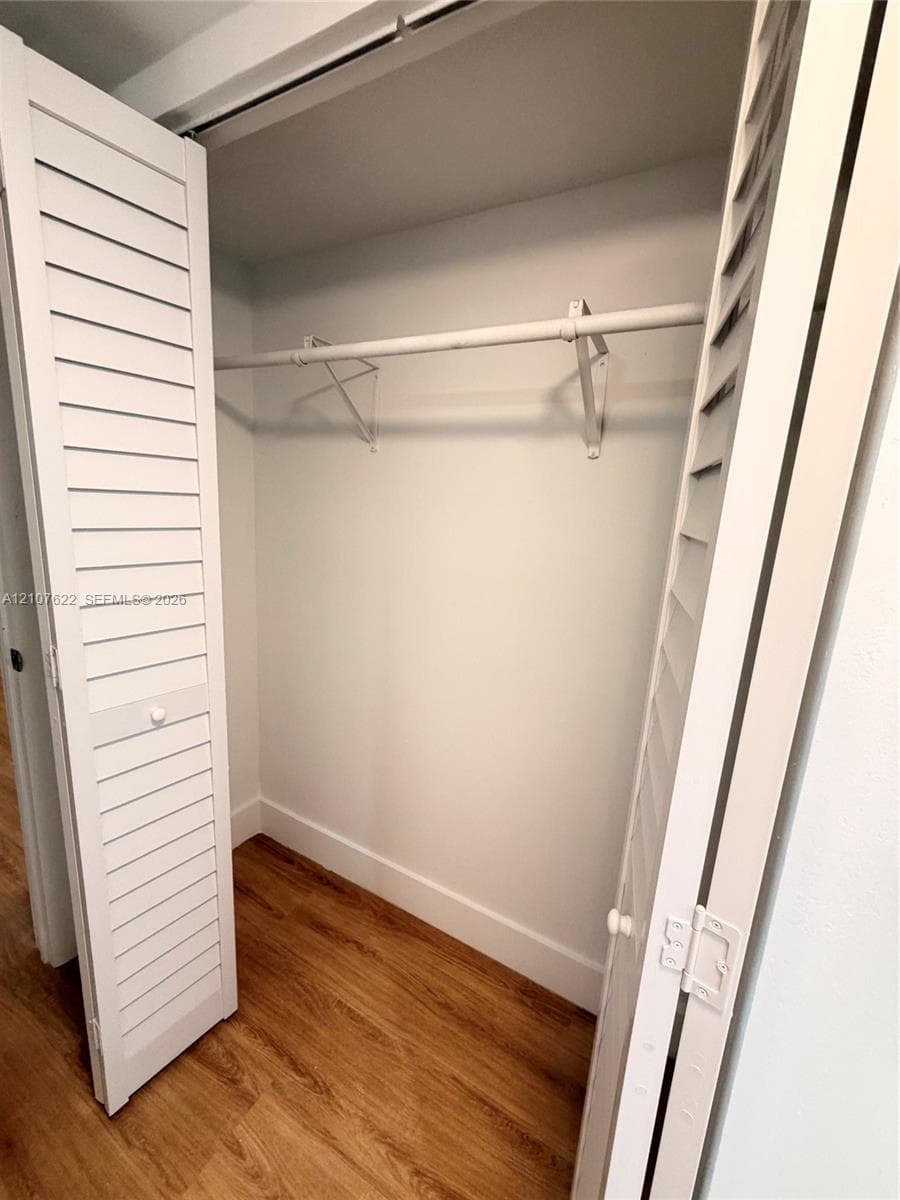 Storage closet featuring white louvered bifold doors, wood-finish flooring, and a metal hanging rod