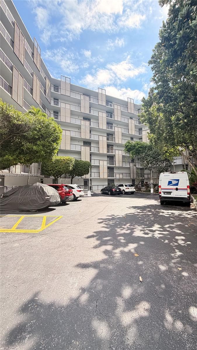 Mid-rise building exterior featuring a white facade, staggered balcony dividers, glass railings, and on-site surface parking