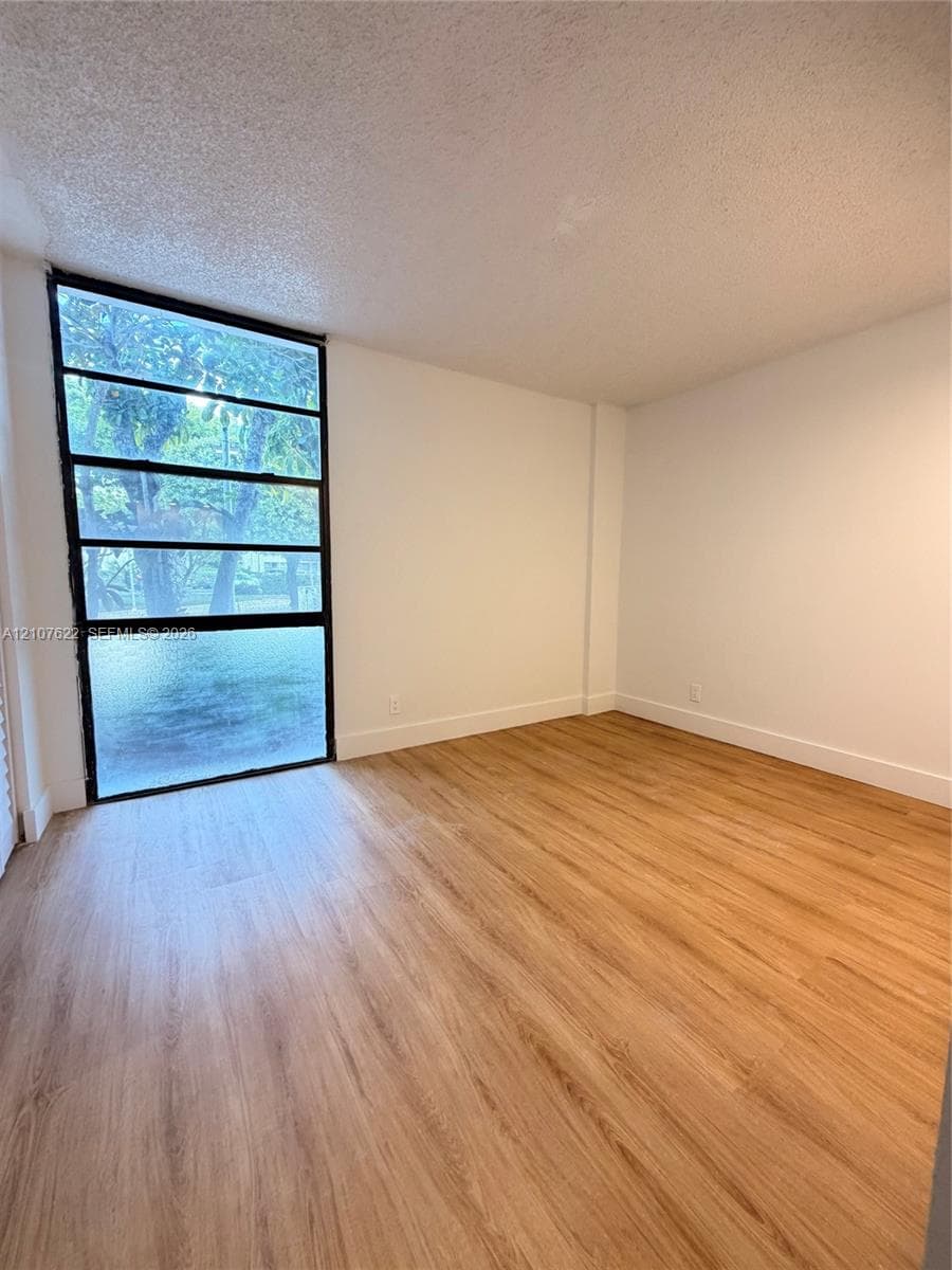 Room interior featuring wood-finish flooring, white walls, and a large multi-pane window with a black frame