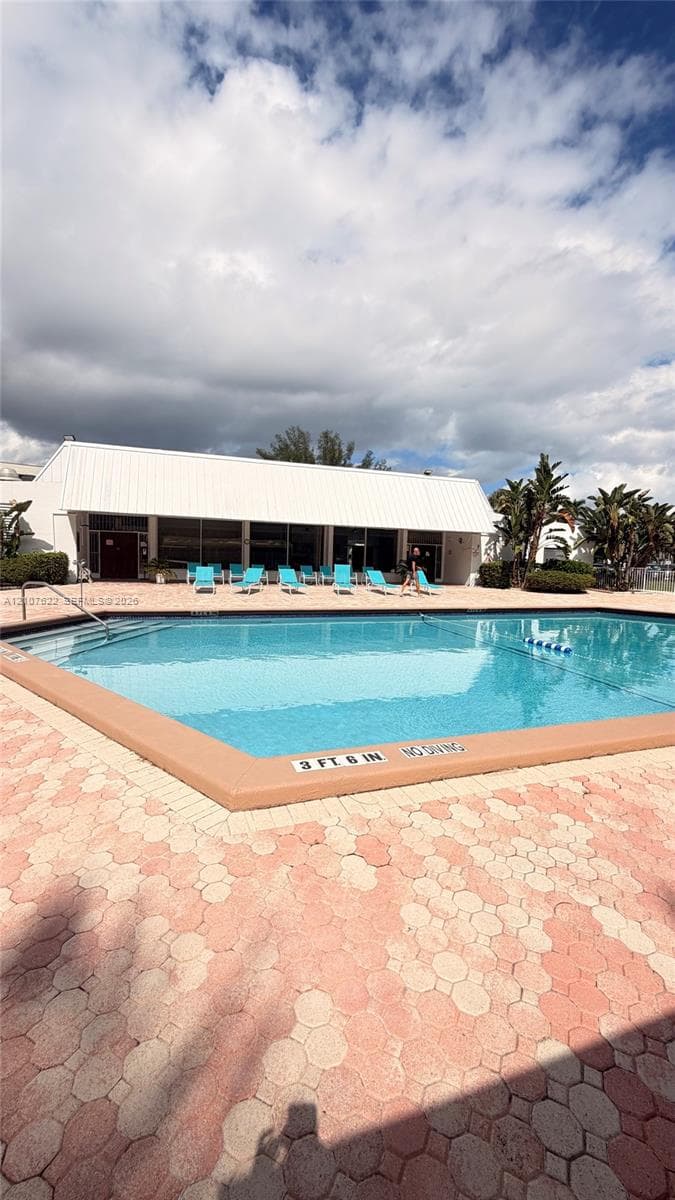 In-ground swimming pool featuring a paved perimeter, metal railings, and a wide-brimmed pavilion roof