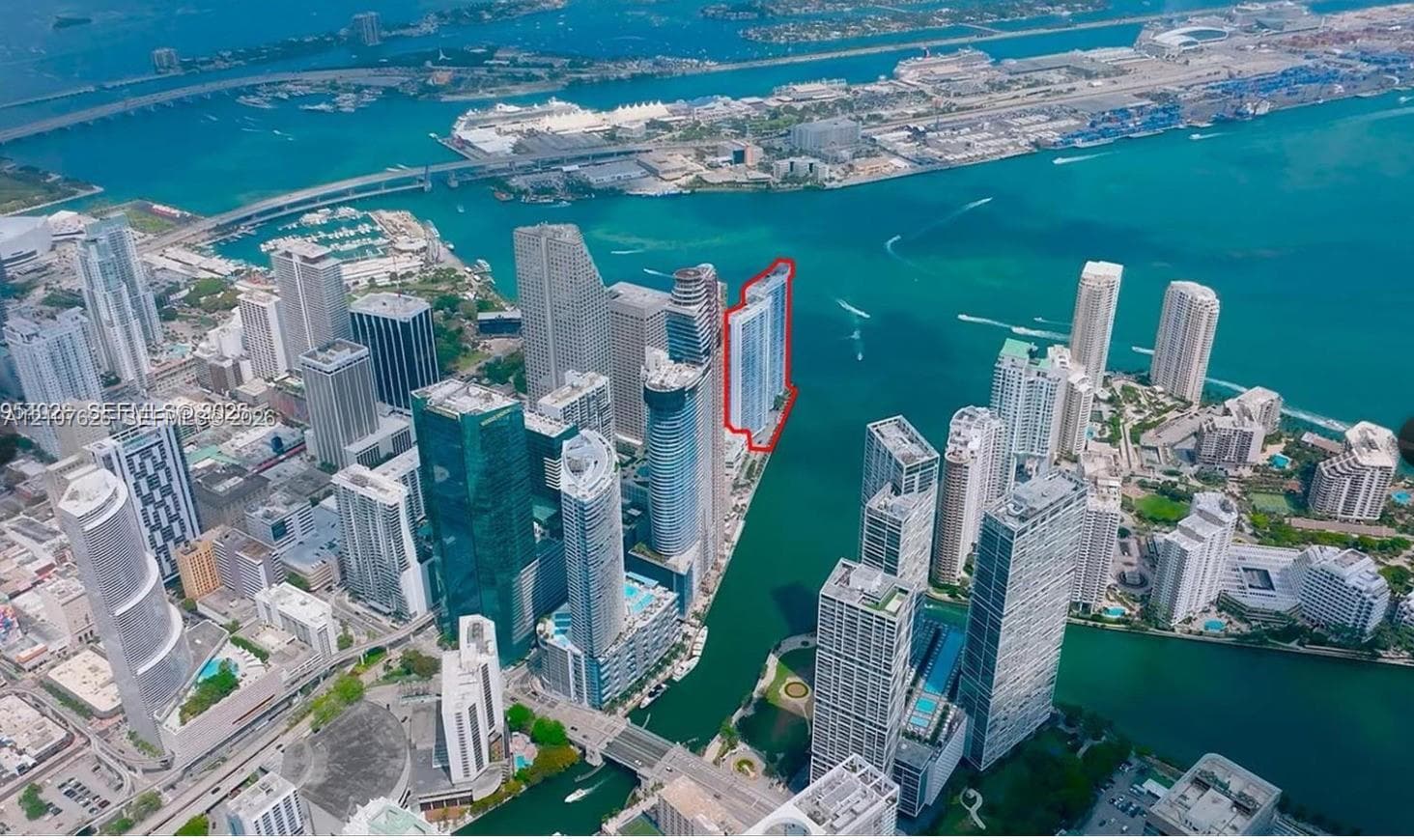 Aerial perspective of a high-rise tower positioned on a waterfront peninsula featuring a glass-facade structure, multiple balconies, and immediate proximity to a harbor