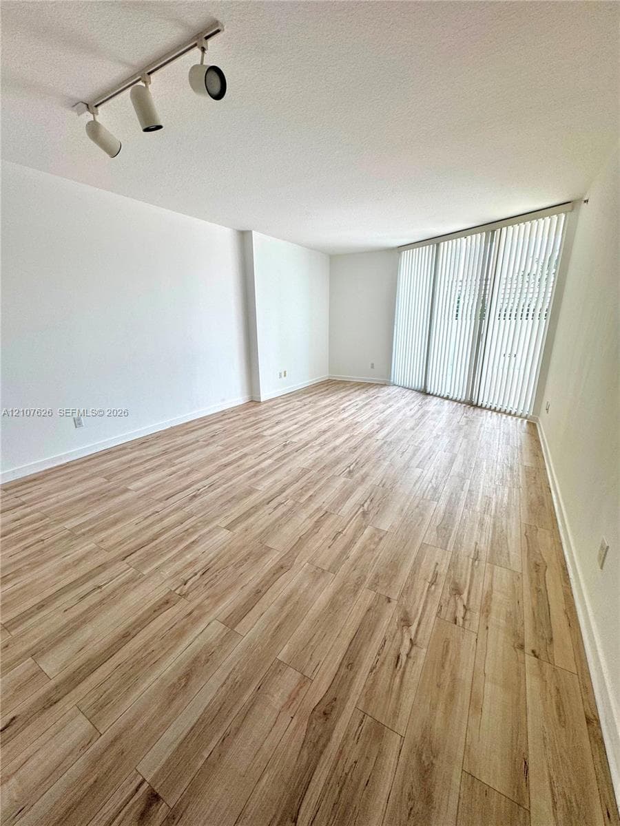 Open interior featuring wood-finish flooring, floor-to-ceiling windows with vertical blinds, and adjustable track lighting