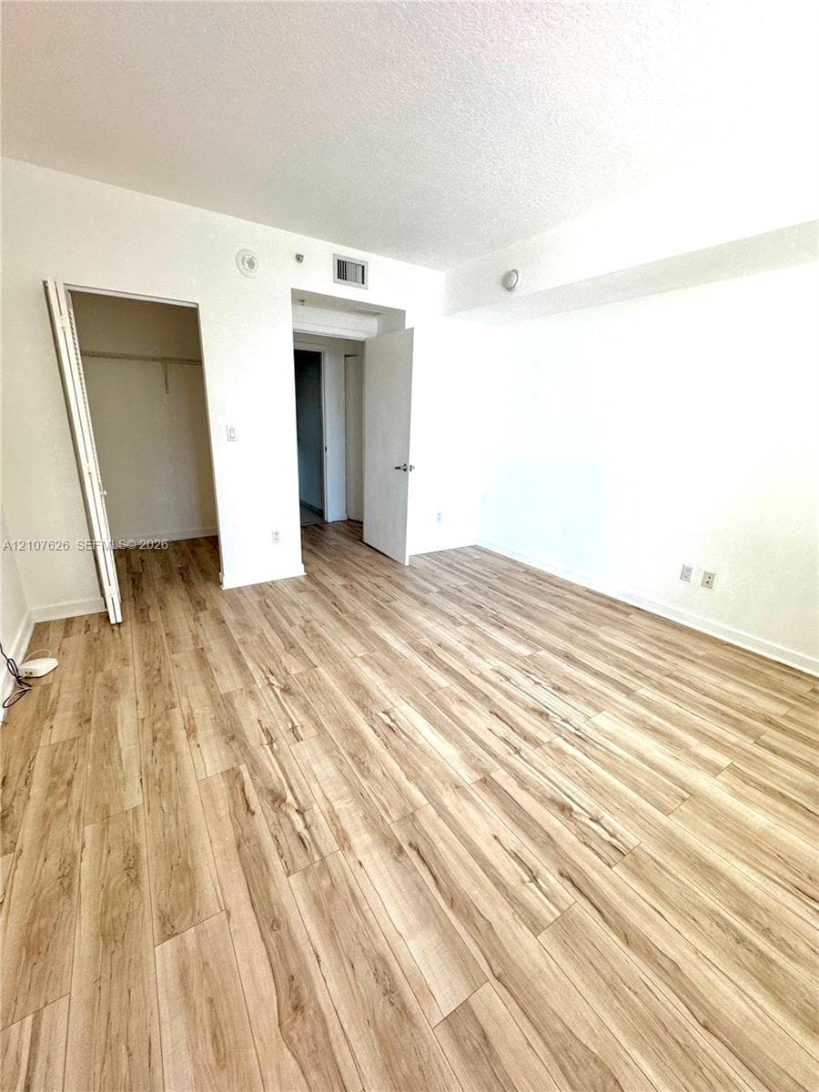 Room featuring wood-finish flooring, white walls, and a closet with a built-in rod