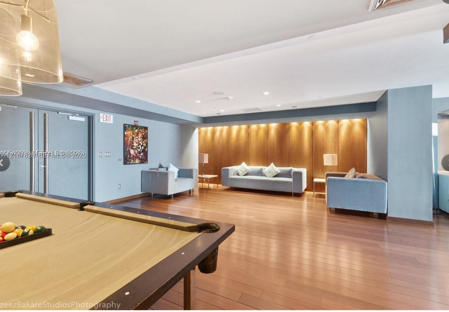Wood-finish flooring, wood-paneled feature wall with integrated recessed lighting, and modern pendant lighting