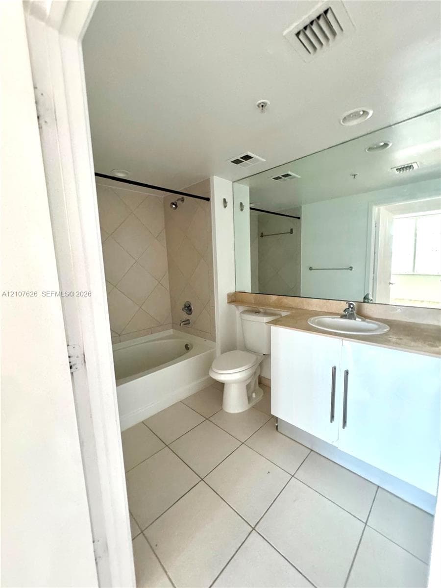 Bright, well-appointed bathroom featuring ceramic tile flooring, a white vanity with dual-sink configuration and wood-finish countertop, recessed ceiling lighting, and an alcove bathtub with tile surround and integrated shower enclosure