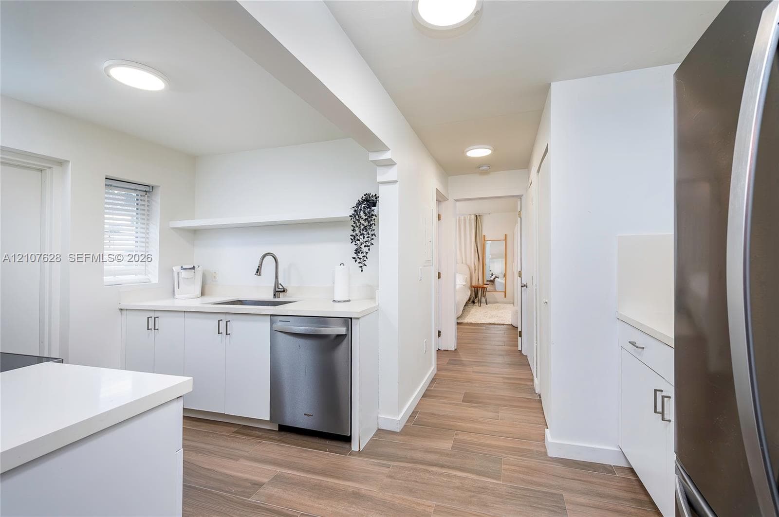 Kitchen featuring white cabinetry, solid-surface countertops, stainless steel dishwasher, wood-finish flooring, and recessed ceiling lighting