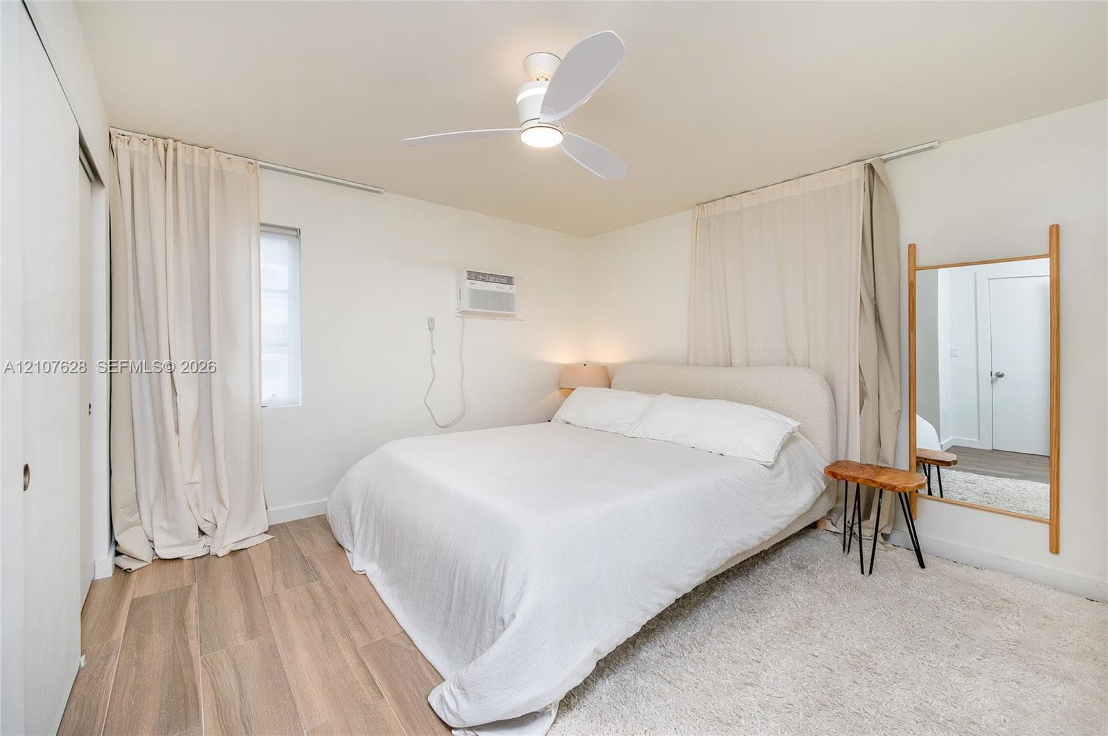 Interior room featuring wood-finish flooring, a contemporary three-blade ceiling fan, and a wall-mounted climate control unit