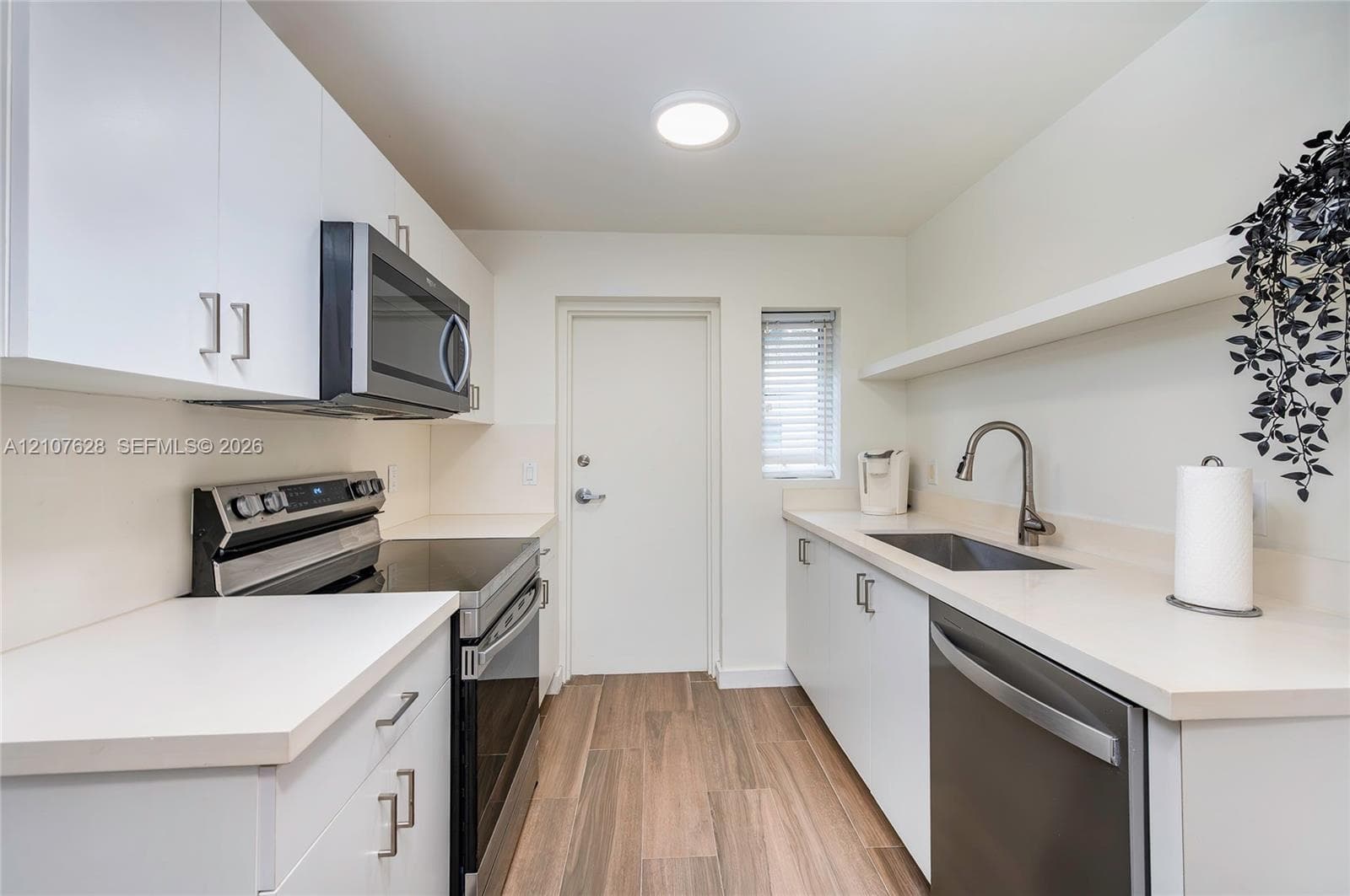 Kitchen featuring white flat-panel cabinetry, stainless steel appliances, solid-surface countertops, a single-basin undermount sink with a gooseneck faucet, and wood-finish flooring