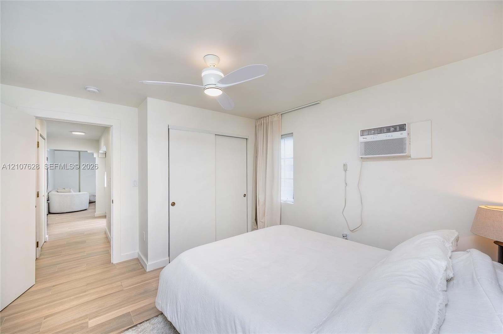 Room featuring wood-finish flooring, a ceiling fan with integrated lighting, a sliding-door closet, and an installed window-mounted air conditioning unit
