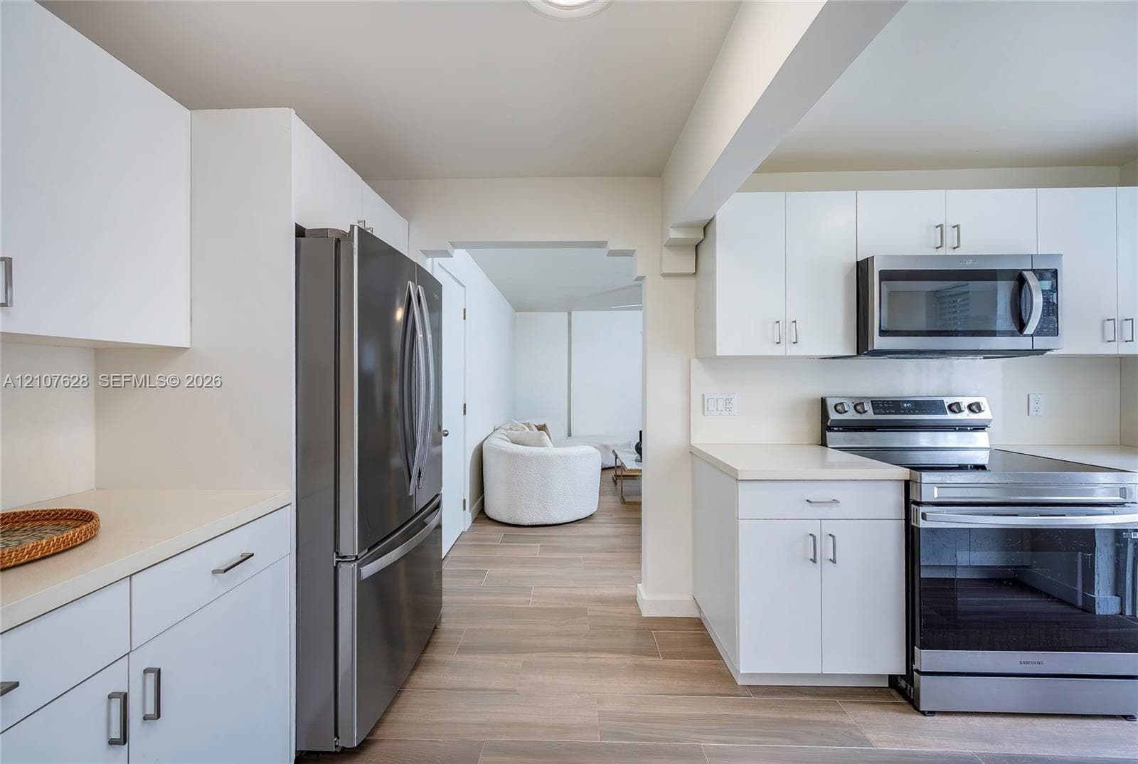Kitchen featuring white cabinetry, stainless steel appliances, wood-finish flooring, and solid-surface countertops