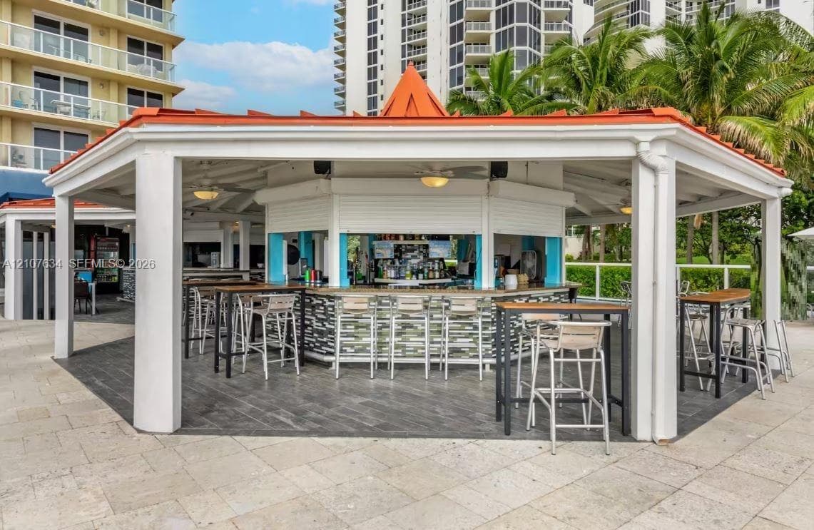 Covered outdoor pavilion featuring a built-in bar, tiled flooring, metal-roofed structure with supporting columns, and recessed lighting
