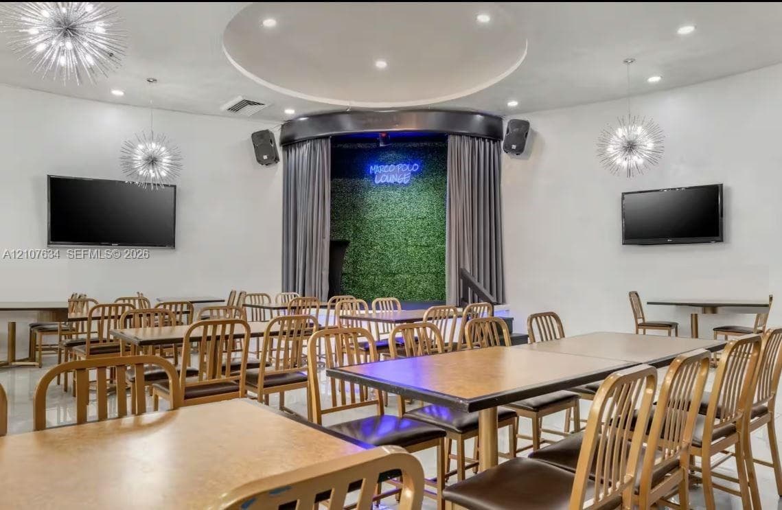 Entertainment space featuring a recessed stage with curtain backdrop, built-in sound system, decorative starburst pendant lighting, and a circular tray ceiling