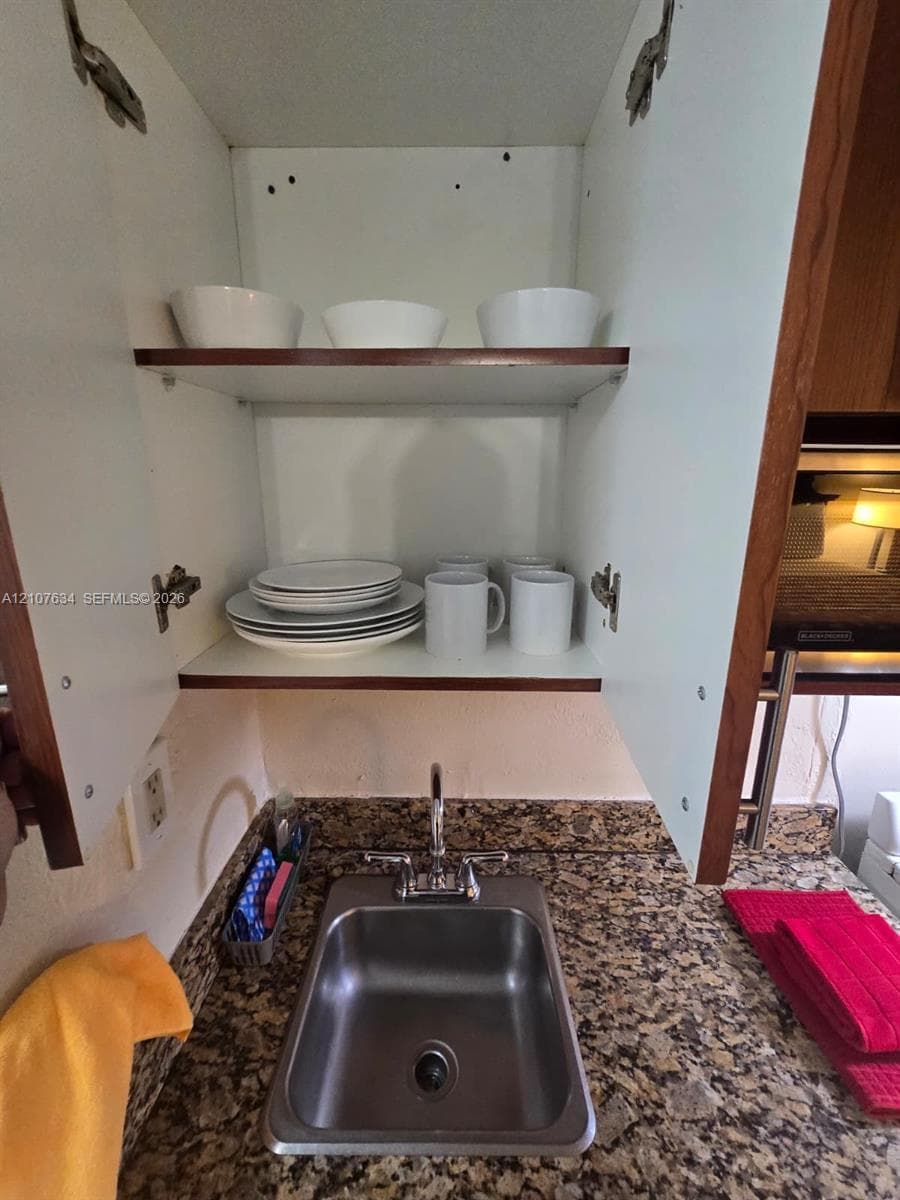 Built-in cabinetry with adjustable shelving, stone-surfaced countertop, and stainless steel drop-in sink with dual-handle faucet